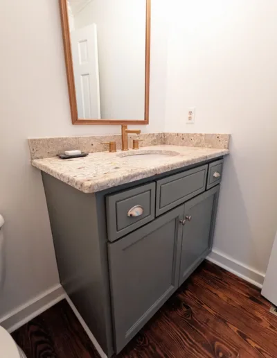 A bathroom with gray cabinets and a mirror.